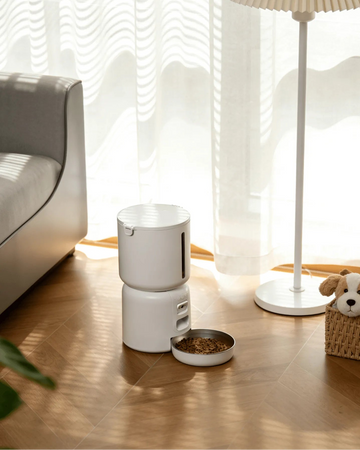 A white smart cat feeder with a camera placed on a wooden floor in a minimalist-style room.